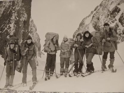 A faded, decades-old photograph of a ski touring group posing on a snowy mountain ridge